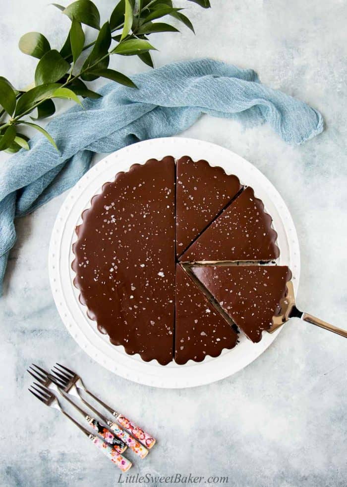 An overhead view of a salted chocolate ganache tart half sliced on a white plate.