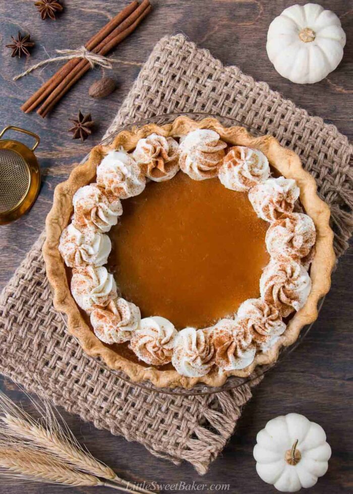 A pumpkin pie topped with whipped cream along the edge on a piece of burlap.