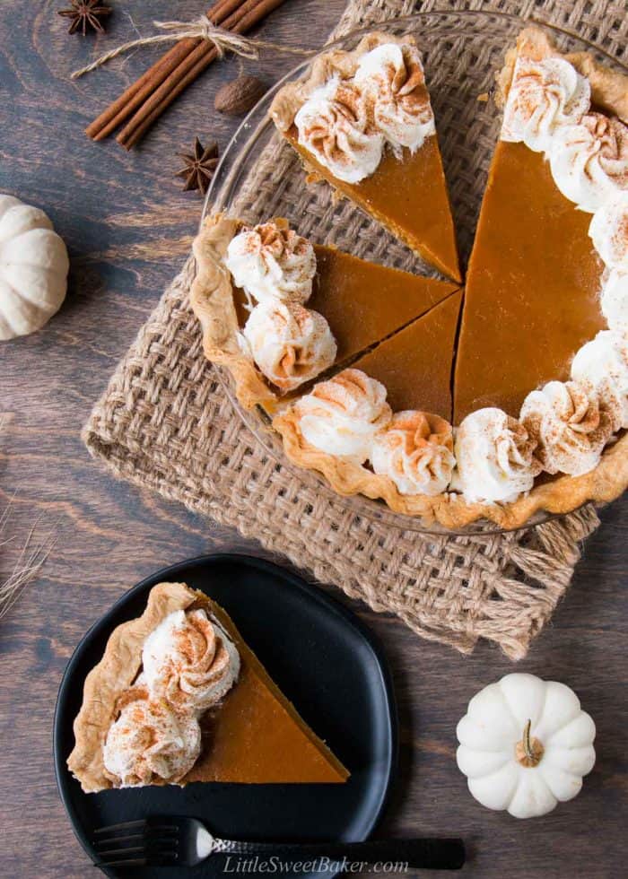 Pumpkin pie with half cut and a slice on a plate.