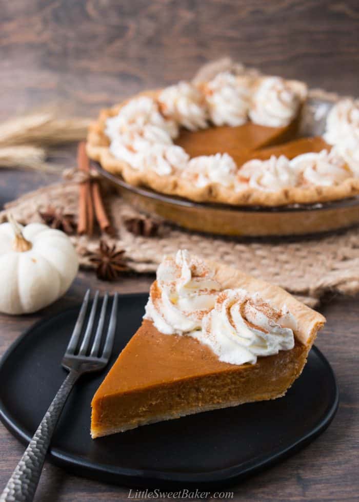 A slice of pumpkin pie with whipped cream on a black plate.