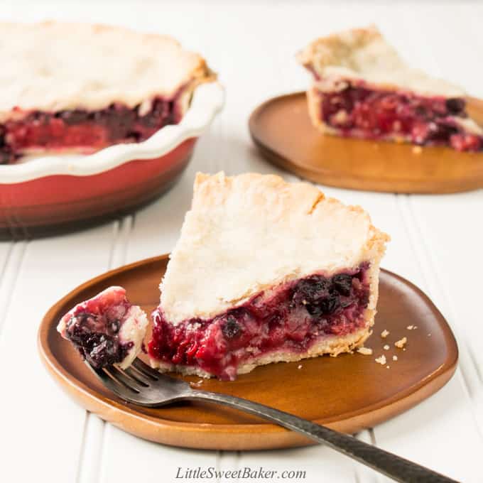 A slice of mixed berry pie on a wooden plate with a piece on a fork.