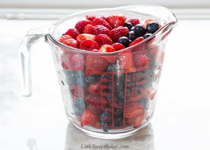 A large measuring cup filled with strawberries, raspberries and blueberries.