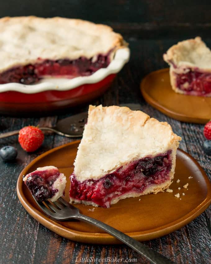 A slice of mixed berry pie on a wooden plate with a piece on a fork.