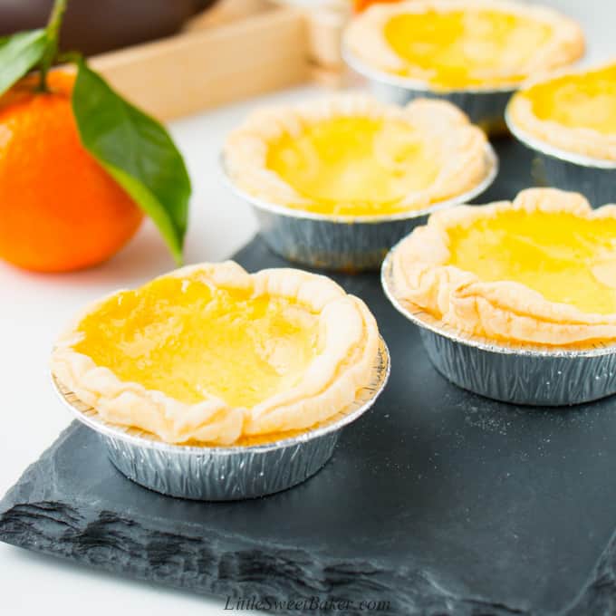 Chinese egg tarts on a black slate board with a mandarin orange in the background.