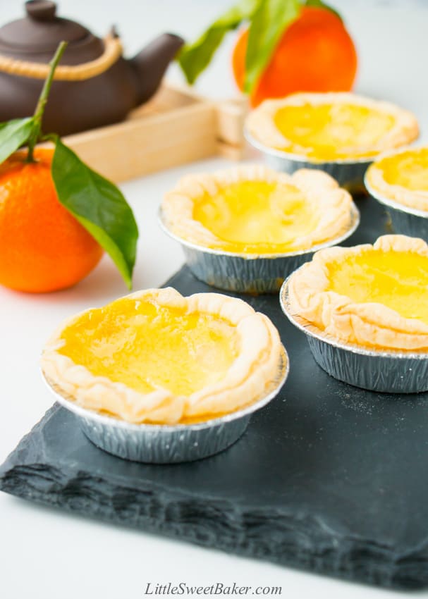 Chinese egg tarts on a black slate with mandarins and a teapot in the background.