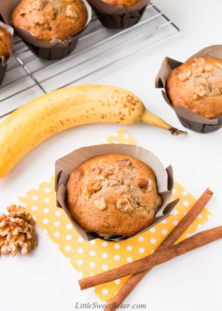 A banana nut muffin on a yellow napkin with two cinnamon sticks, banana, and walnuts.