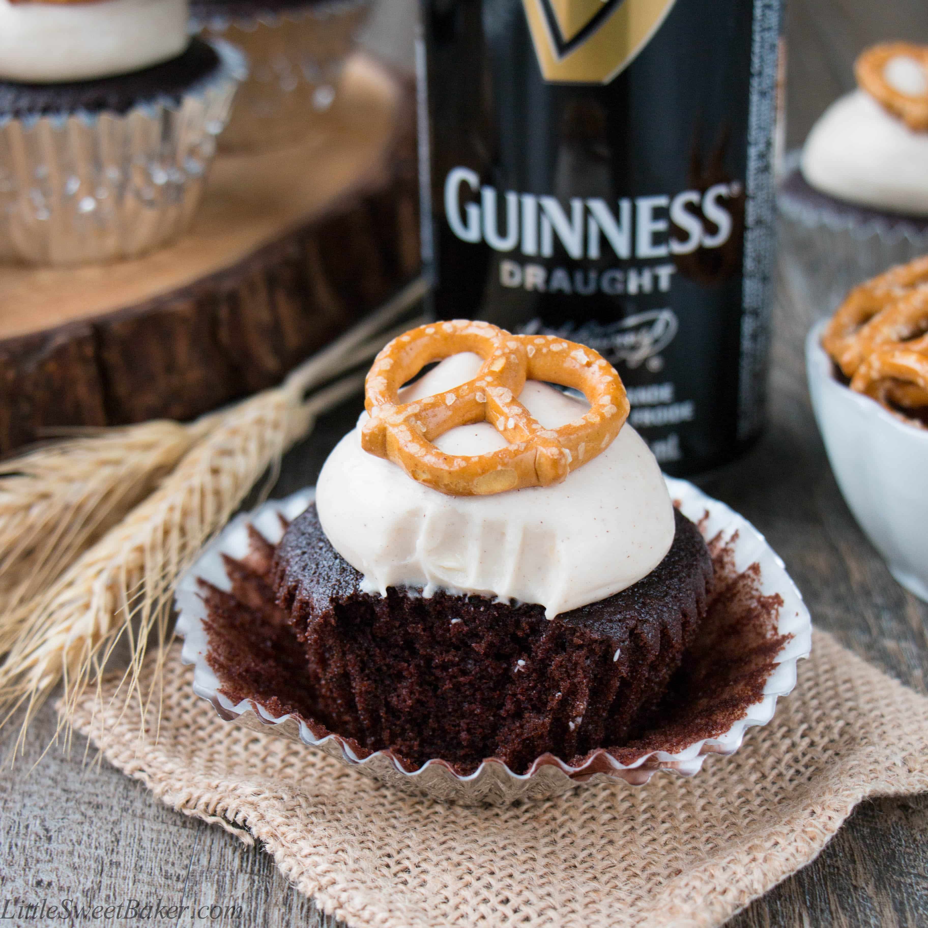 A Guinness cupcake topped with cream cheese frosting and pretzel with a bite taken out.