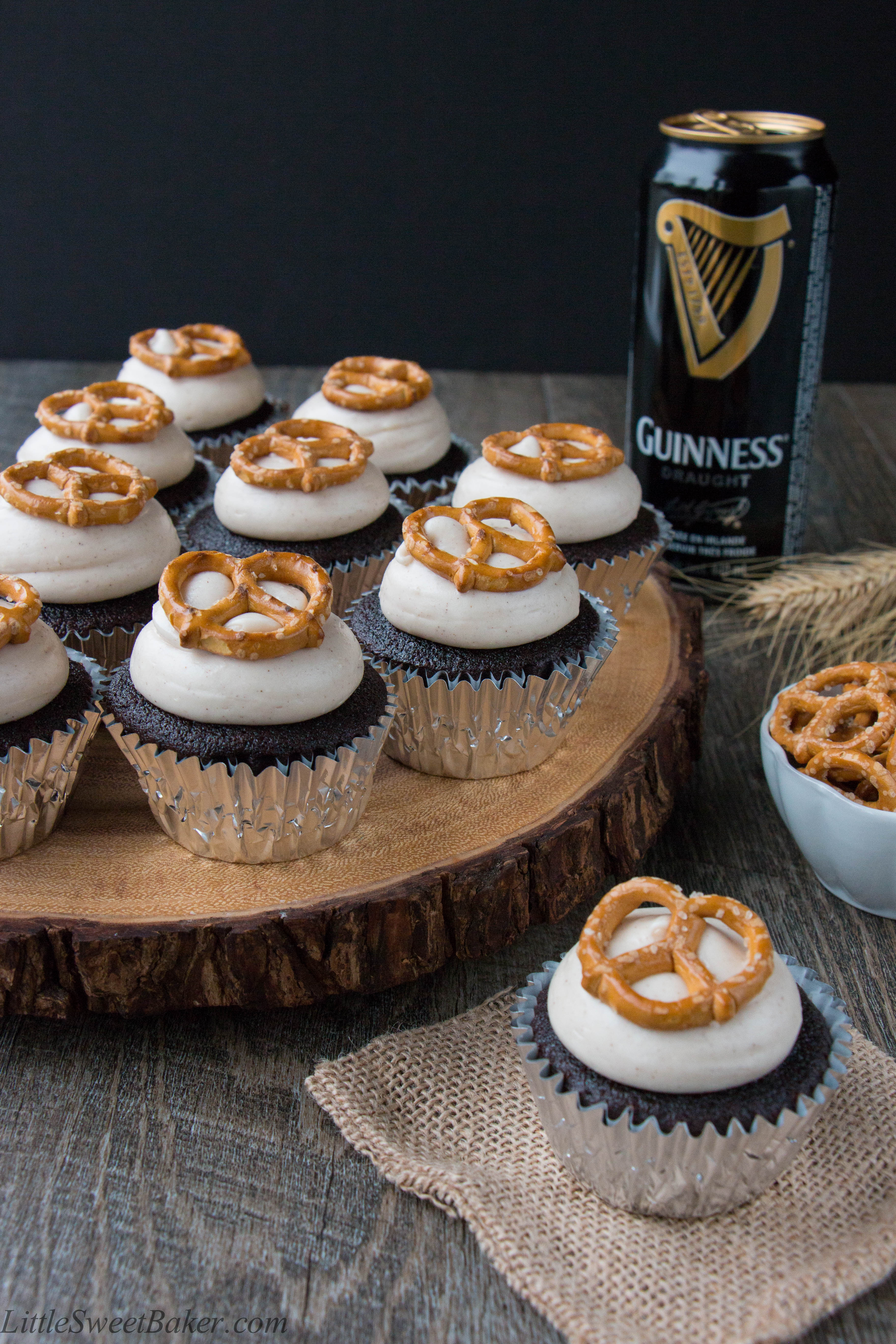 Guinness cupcakes topped with cream cheese frosting on a wooden live edge serving board.