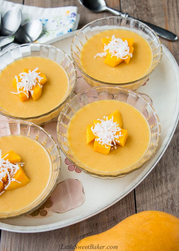 Four bowls of mango pudding topped with diced mangoes and coconut on a plate.