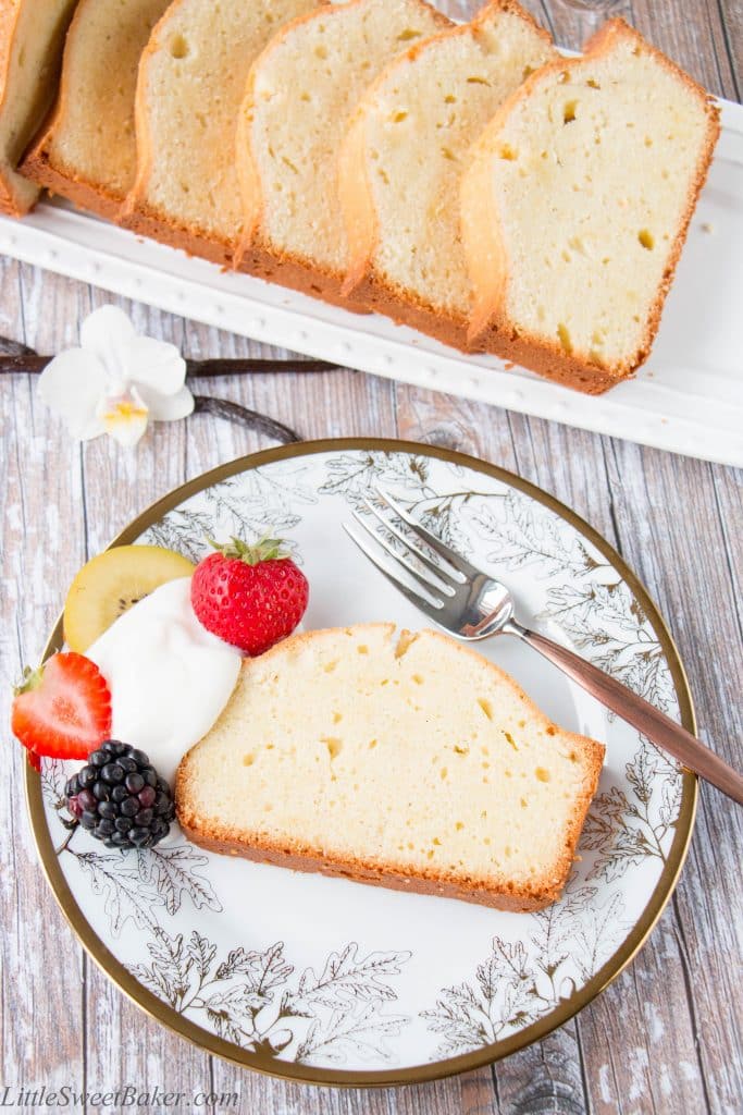 A slice of vanilla pound cake on a white and gold plate with berries and yogurt.