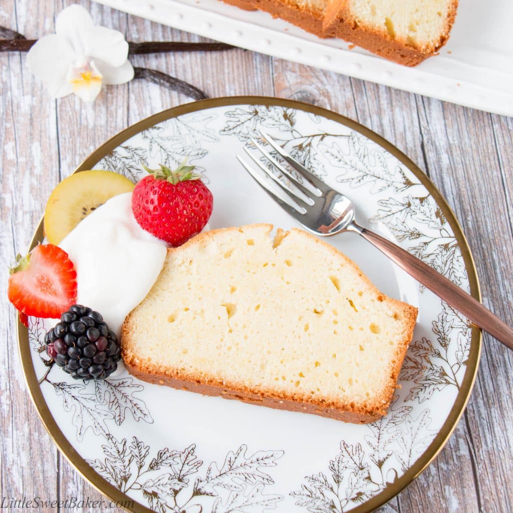 A slice of classic pound cake on a white and gold plate with berries and yogurt.