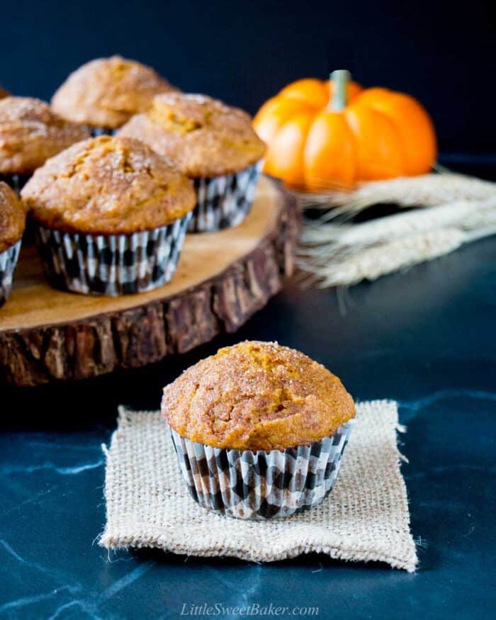 A pumpkin spice muffin on a piece of burlap with a wooden tray of muffins behind.