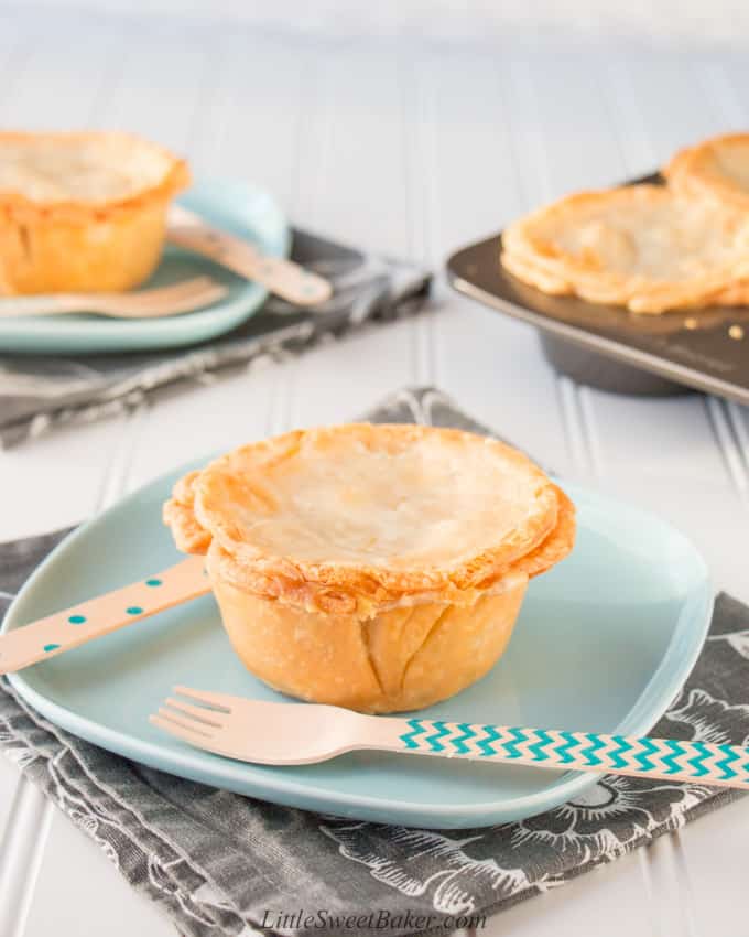 Mini turkey pot pies on a teal plate with wooden cutlery on grey napkins.