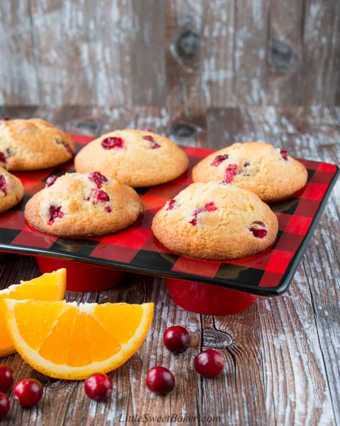 cranberry orange muffins in a red and black ceramic muffin pan with orange wedges and cranberries