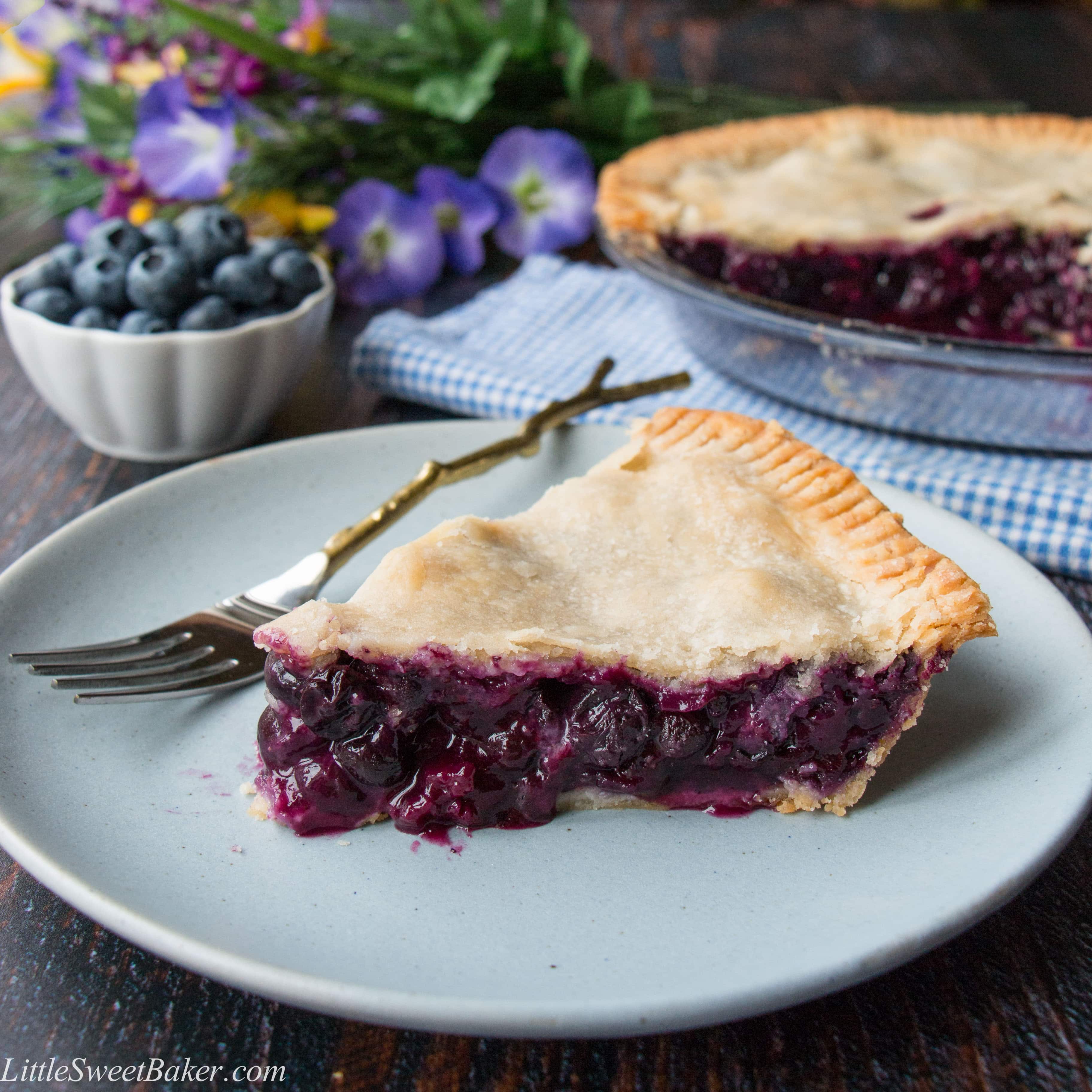 A slice of blueberry pie on a blue plate with a gold fork