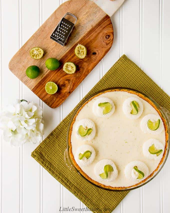 Overhead shot of a key lime pie on a green dish towel and a cutting board with key limes.