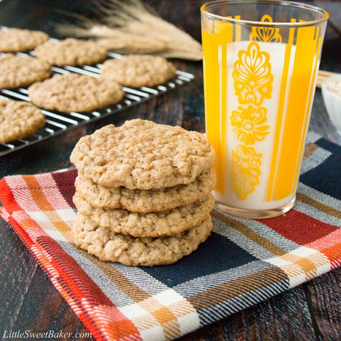 A stack of oatmeal cookies on a plaid napkin with a glass of milk.