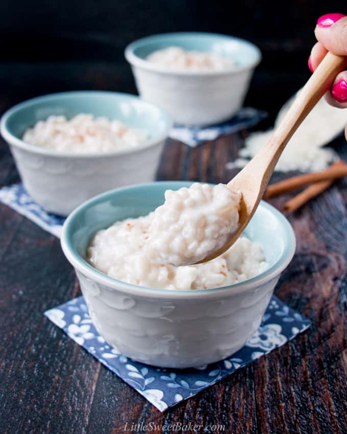 A hand holding a spoon of rice pudding with bowls of rice pudding in the background.