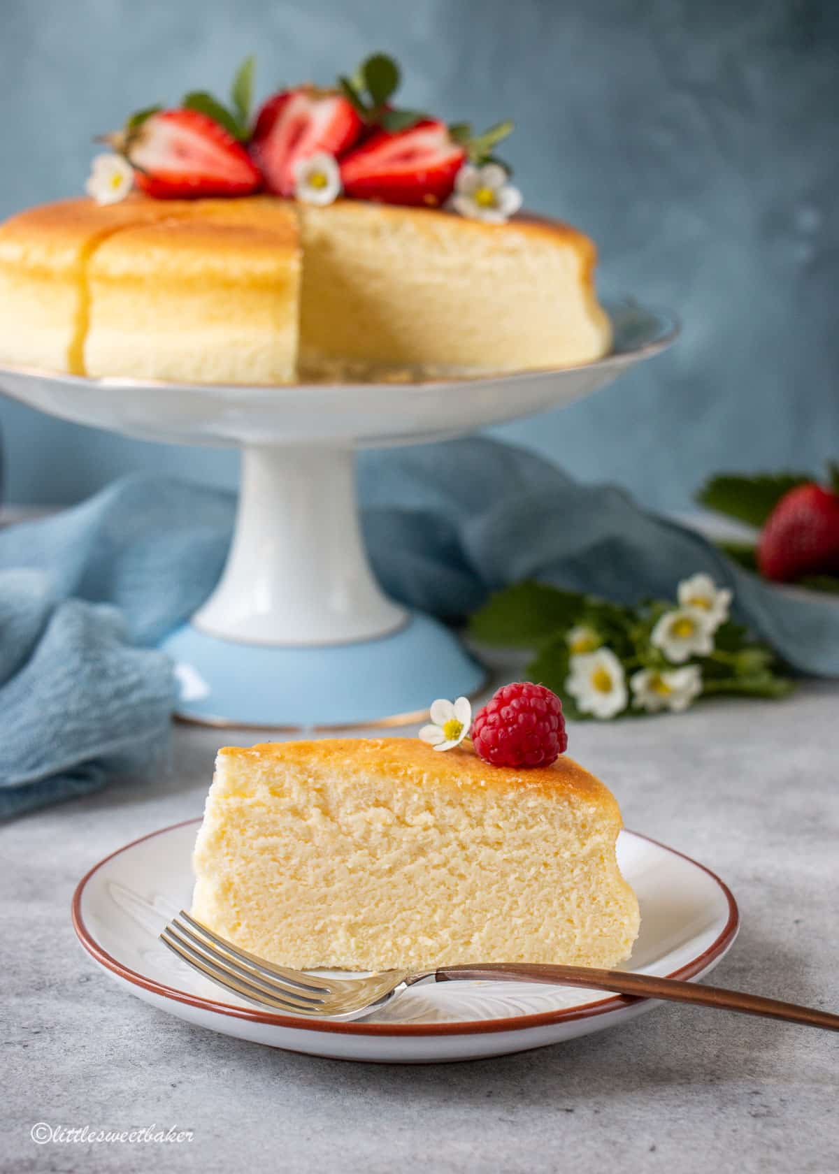 A slice of Japanese cheesecake on a plate with the rest of the cheesecake in the background.