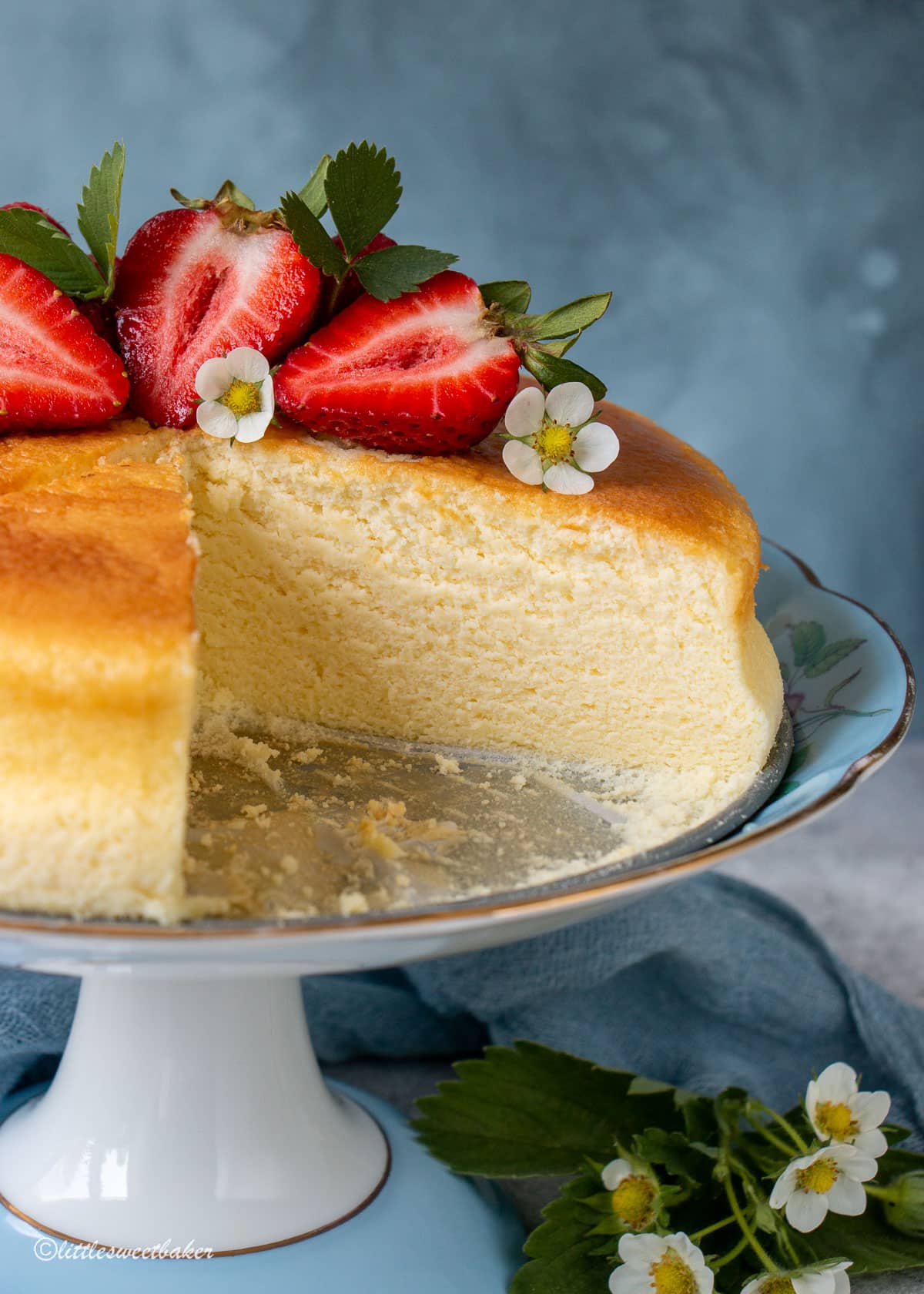 Japanese cheesecake topped with strawberries on a cake stand with a quarter of it removed.