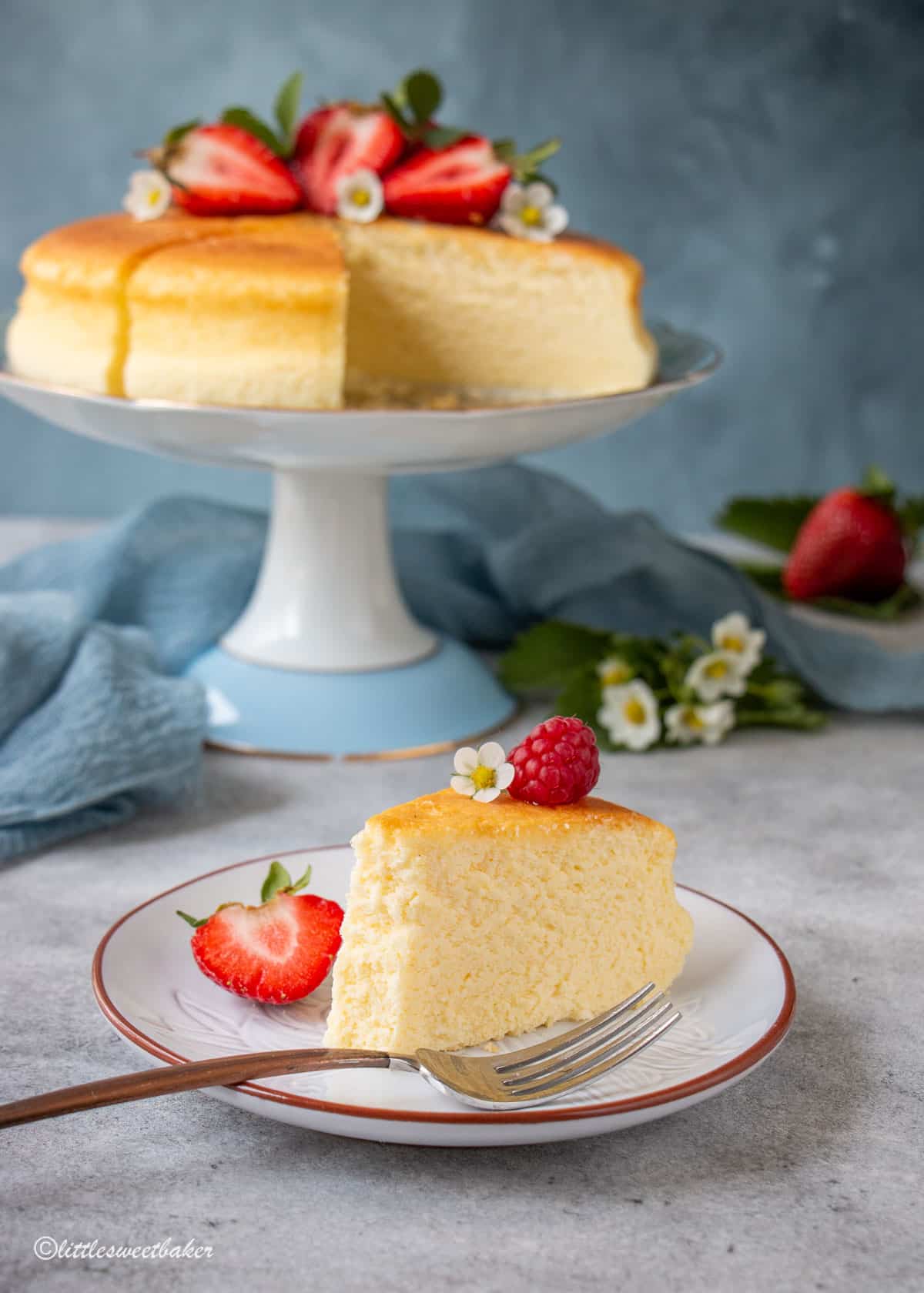 A slice of cotton cheesecake on a plate with a piece missing and the rest of the cake in the background.