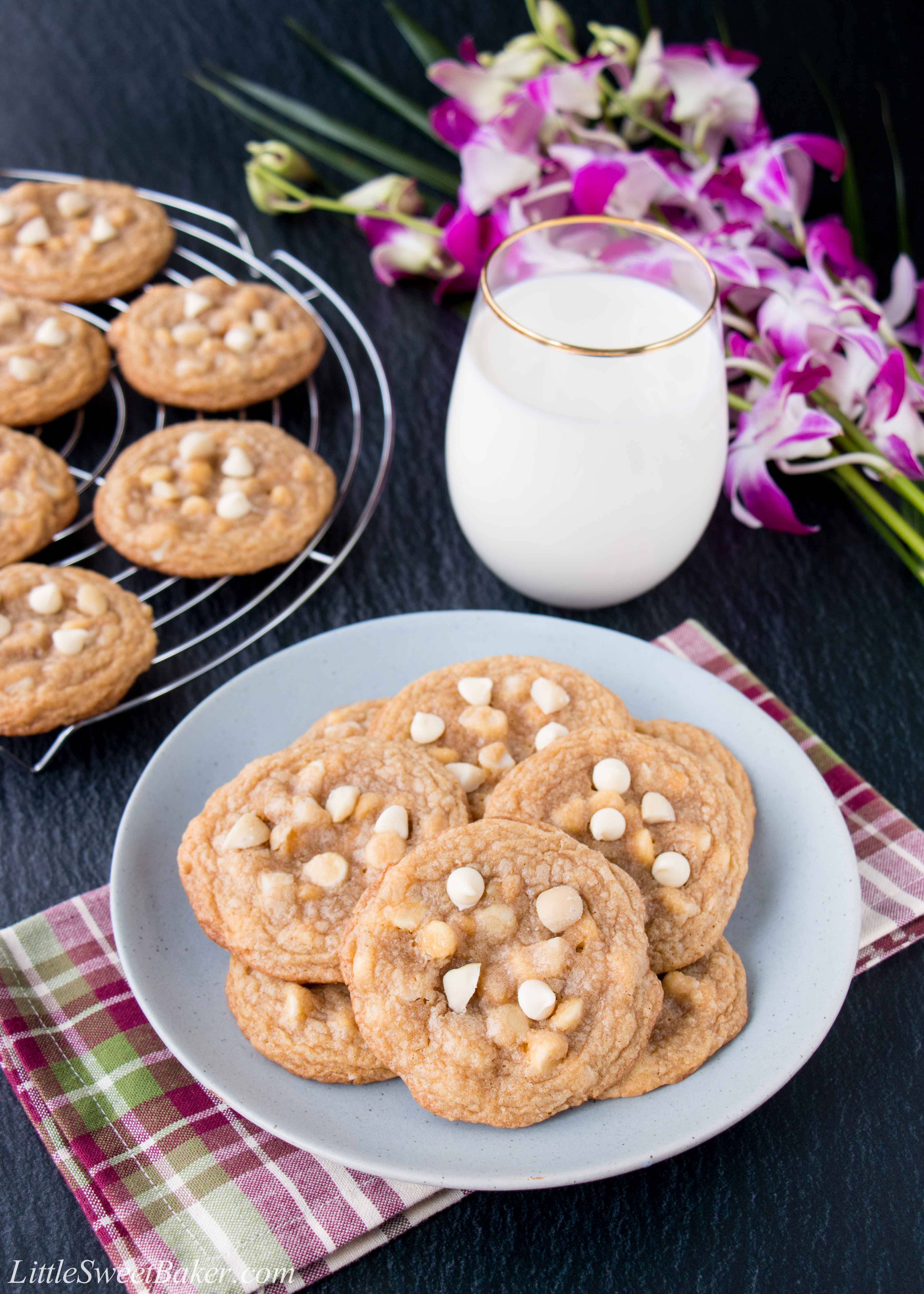 A plate of white chocolate macadamia nut cookies with a glass of milk and flowers.
