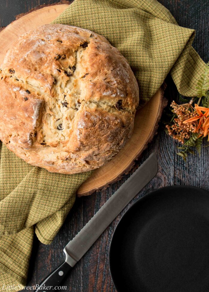 A loaf of Irish soda bread on a green dish towel and a wooden board.