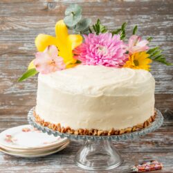 Coated in a delicious cream cheese frosting, this supremely moist banana cake has sweet pieces of pineapples and crunchy pecans mixed in. It's spiced with cinnamon and nutmeg, and sweetened with brown sugar. #hummingbirdcake #layercake #creamcheesefrosting #bananacake