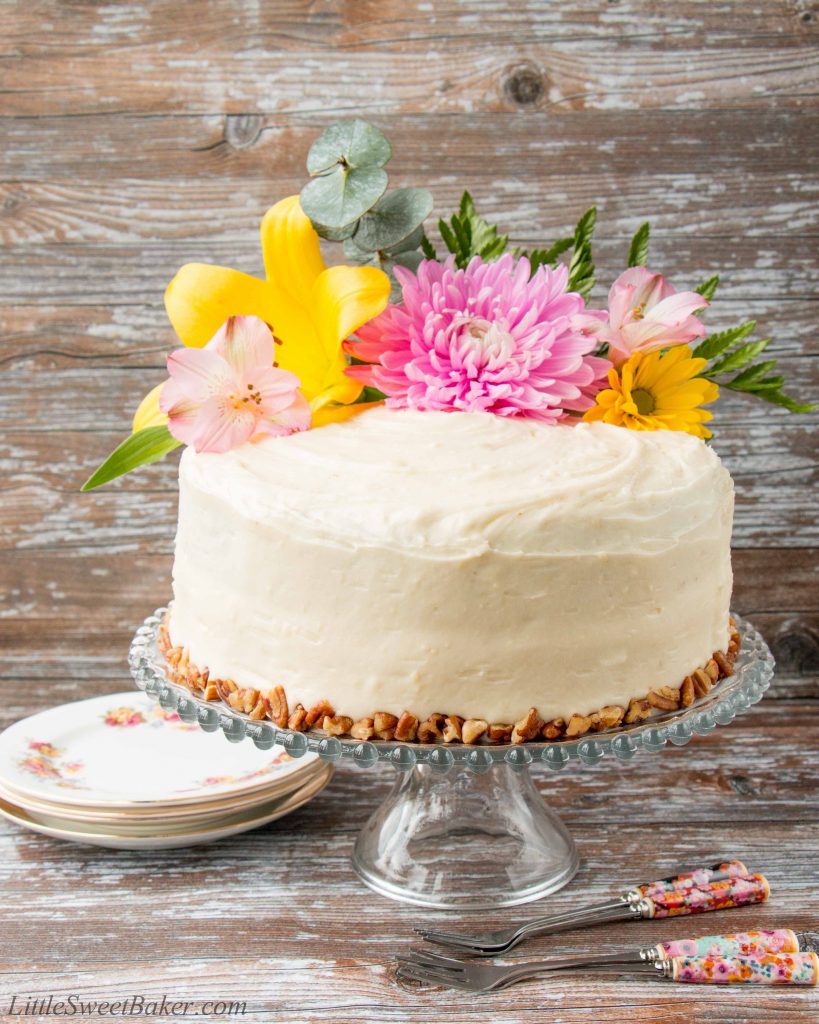 Coated in a delicious cream cheese frosting, this supremely moist banana cake has sweet pieces of pineapples and crunchy pecans mixed in. It's spiced with cinnamon and nutmeg, and sweetened with brown sugar. #hummingbirdcake #layercake #creamcheesefrosting #bananacake