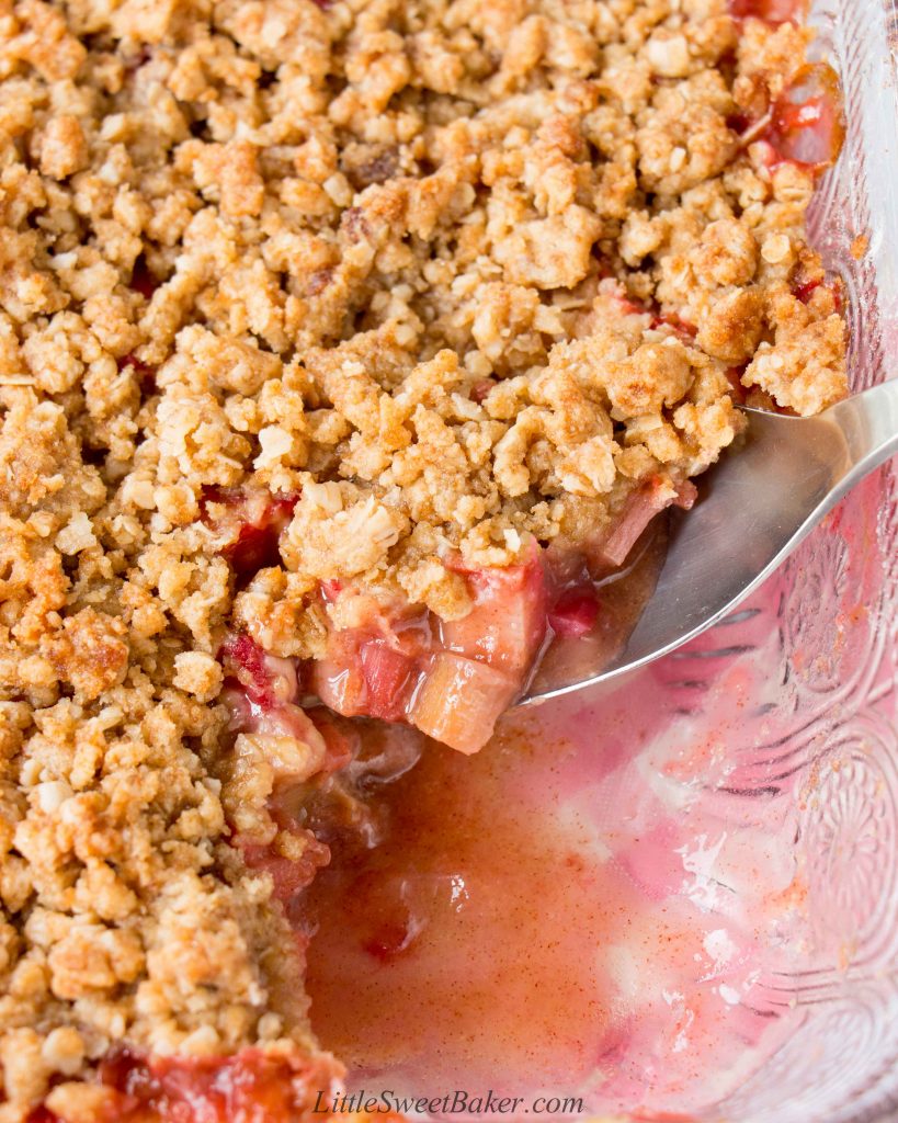 A spoon of rhubarb crisp being lifted from a glass dish.