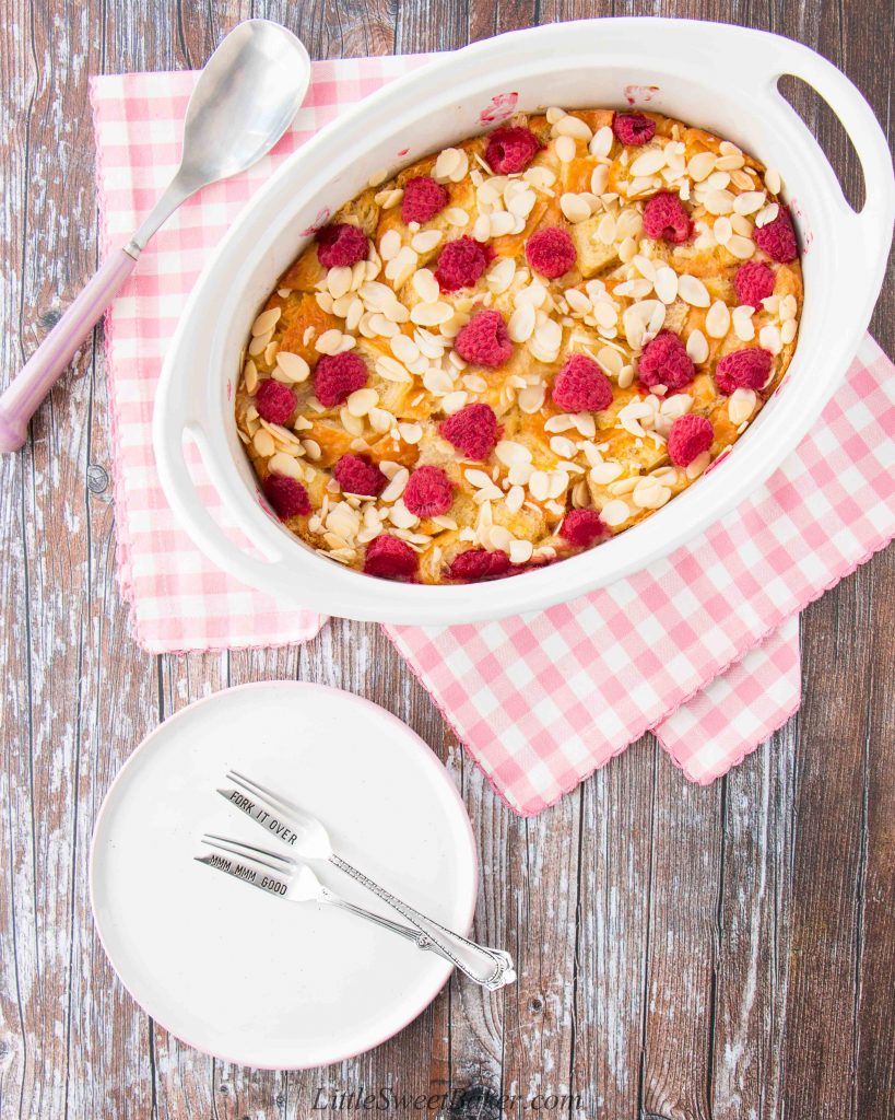 Croissant bread and butter pudding with raspberries and sliced almonds in a white casserole dish.