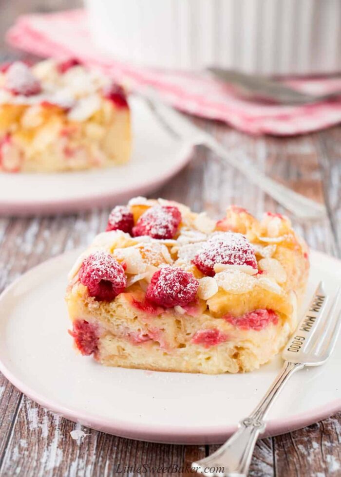 A slice of croissant bread pudding with raspberries and almonds on a white and pink plate.