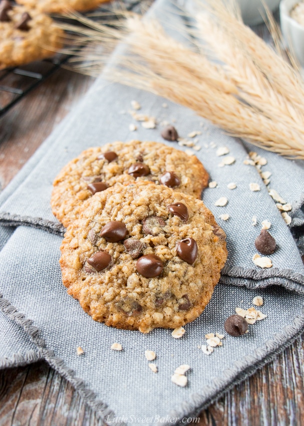 Two oatmeal chocolate chip cookies on a blue-grey cloth napkin