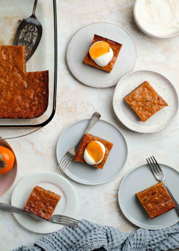 Five slices of persimmon pudding on plates, two topped with whipped cream and persimmon slices.