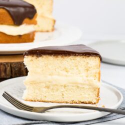A slice of Boston cream pie on a light grey plate with fork.