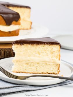 A slice of Boston cream pie on a light grey plate with fork.