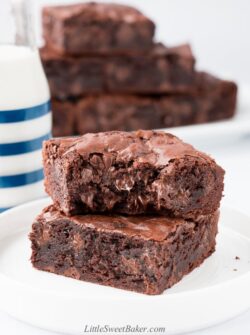 A stack of two brownies on a white plate with a bite taken out of the top one.