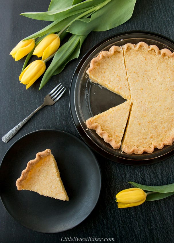 A lemon pie and slice on a black plate with yellow tulips and a dark grey fork.