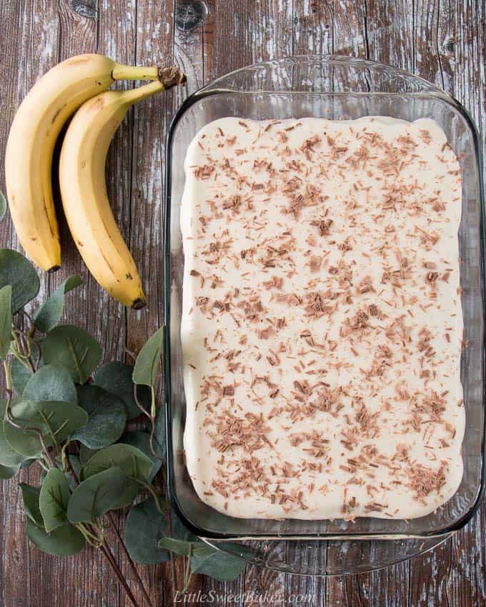 An overhead view of a banana cake topped with cream cheese frosting and chocolate shavings.