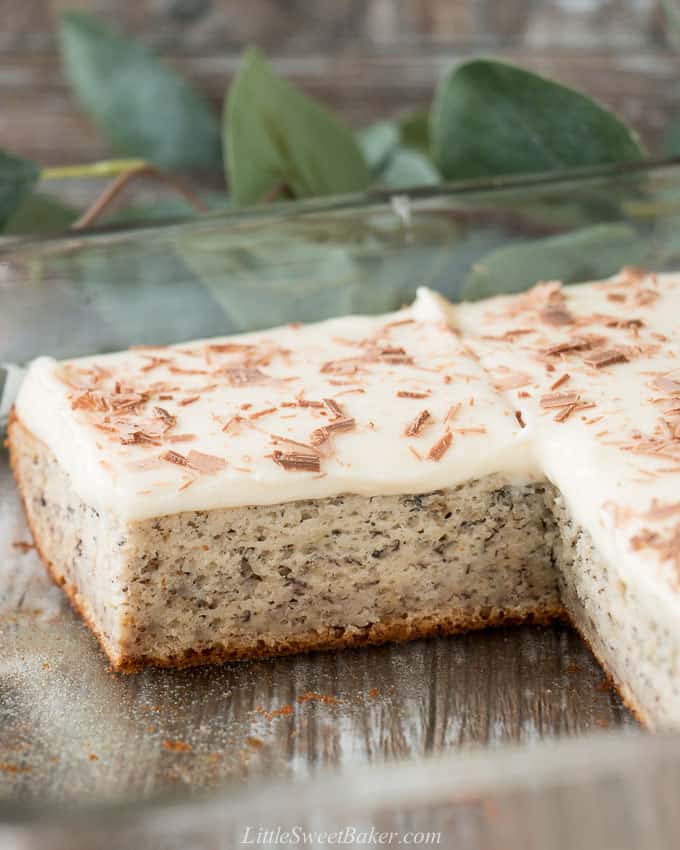 A cut piece of banana cake with cream cheese frosting in a glass baking pan.