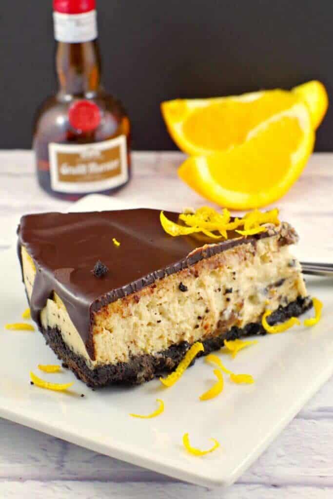 a slice of grand marnier cheesecake with chocolate glaze and orange zest on a white plate