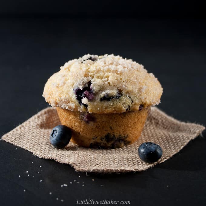 A blueberry streusel muffin on a piece of burlap with two blueberries.