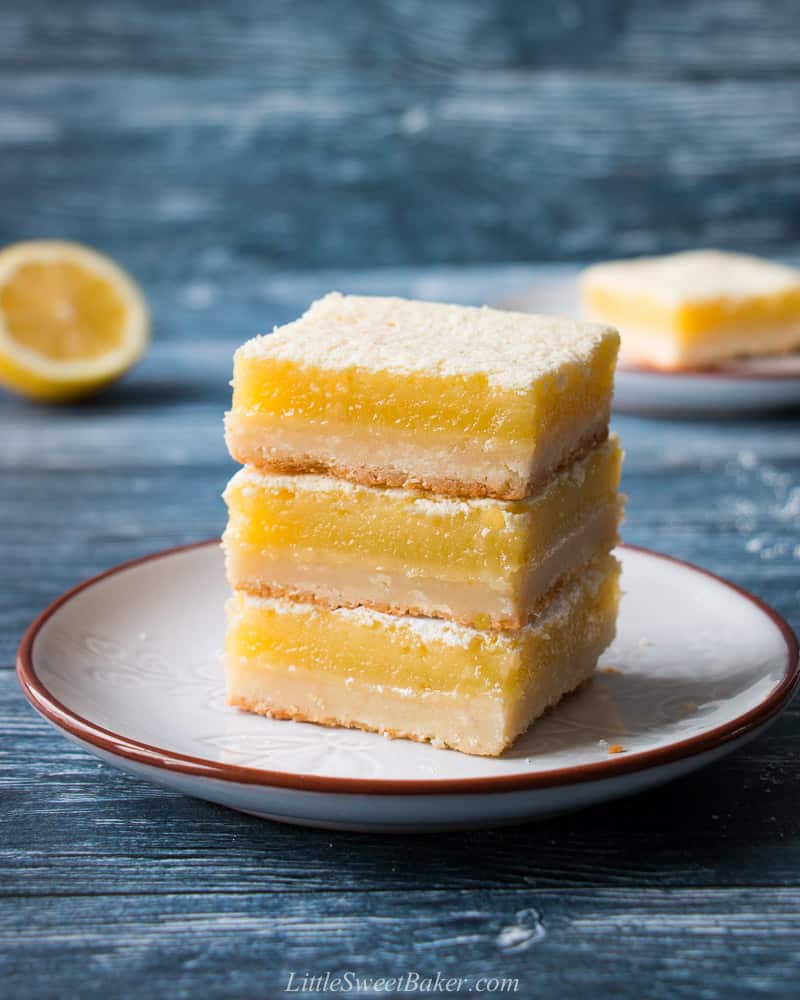 A triple stack of lemon bars on a light gray plate with a blue background.