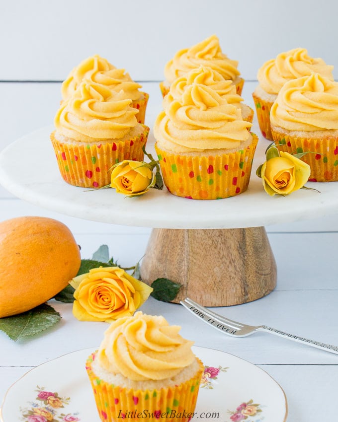 Mango cupcakes on a marble cake stand with yellow roses.