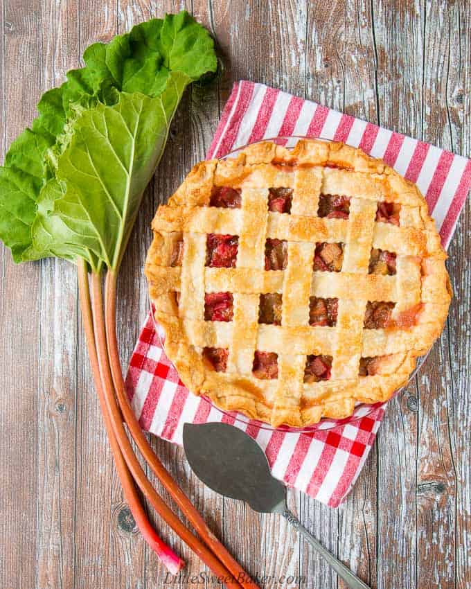 A rhubarb pie on a red and white dish towel with a couple of stalks of rhubarb beside it.
