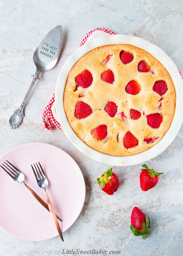 A whole strawberry cake with a pink plate, forks, cake serve and strawberries.