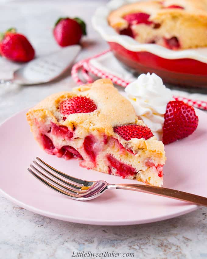 Slice of strawberry cake on a pink plate with fork and whipped cream.