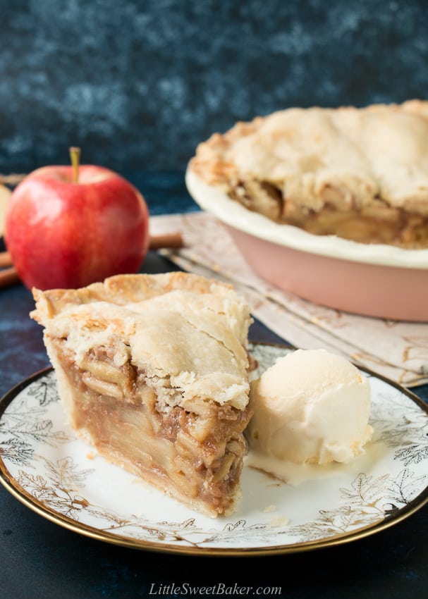 A slice of deep dish apple pie with icecream on a white and gold plate