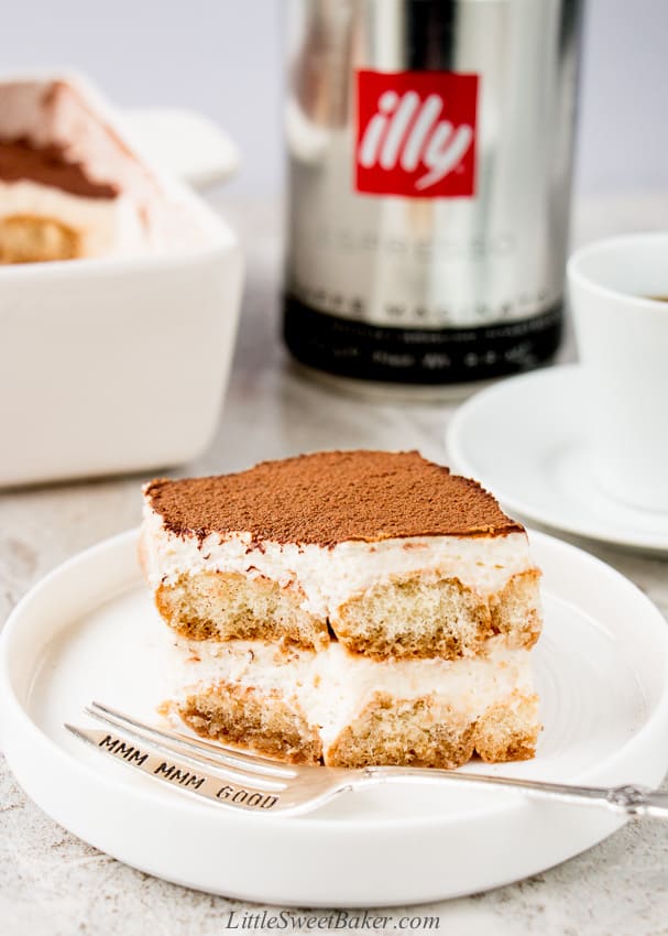 A slice of eggless tiramisu with a piece missing on a white plate with a silver fork.