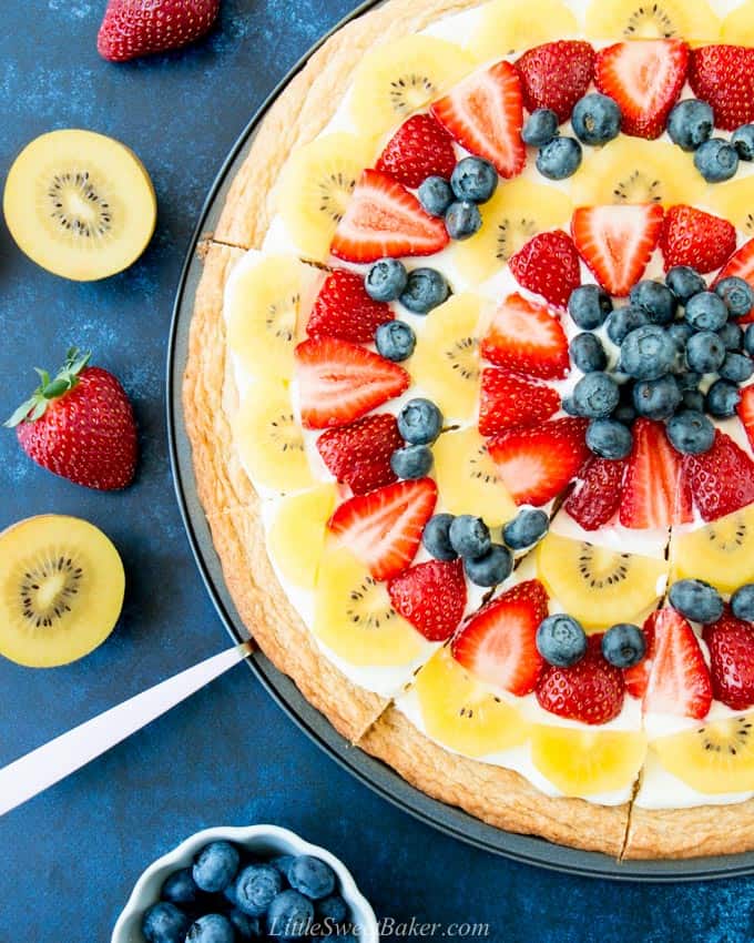 A close-up of a fruit pizza with slices cut.